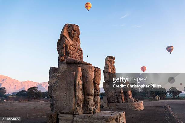 Hot air balloons transporting tourists float over the Colossi of Memnon which marks the eastern entrance of the Amenhotep III Temple in Thebes. Today...