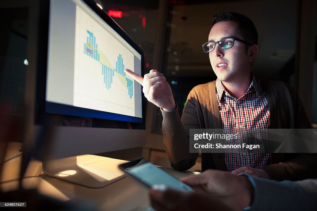 Coworker discussing findings on screen at night