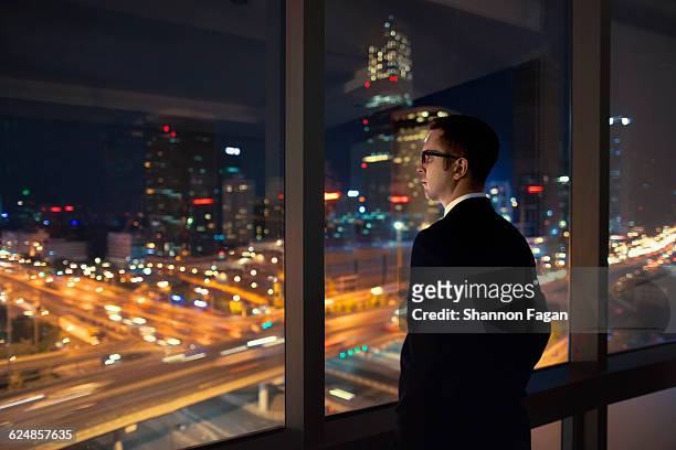 young man looking out of window at night - fensterfront innen stock-fotos und bilder