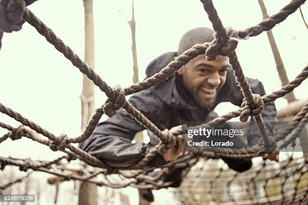 schwarzer hübscher junger mann klettert beim schlammlauf über hindernis - hindernisparcours stock-fotos und bilder