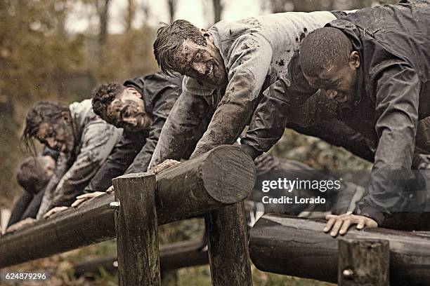 multiétnico equipo de lodo correr de hombres que suben a lo largo de la carrera de obstáculos - campamento de instrucción militar fotografías e imágenes de stock