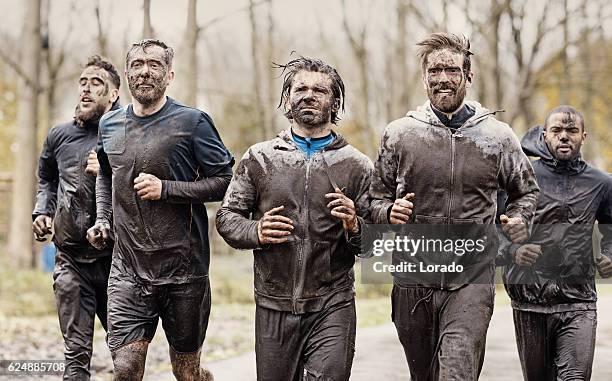 multiethnic mud run team of men running during obstacle course - mud runner stock pictures, royalty-free photos & images