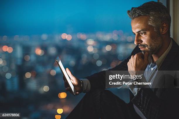 businessman looking at digital tablet at night - handelaar financieel beroep stockfoto's en -beelden