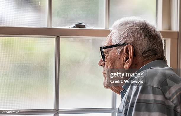 wistful senior man staring through hazy window - smart windows stockfoto's en -beelden