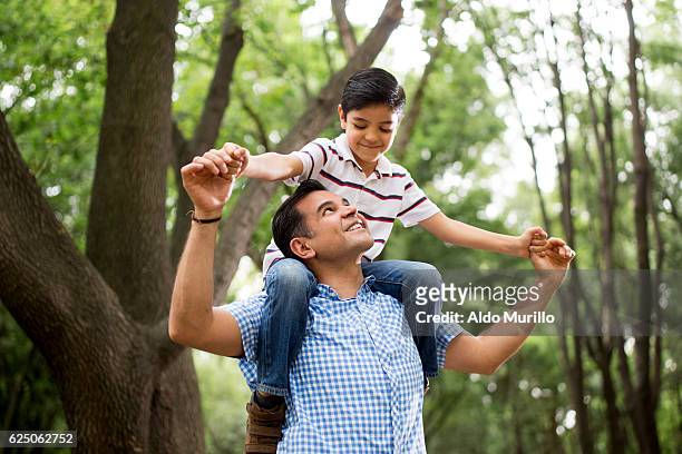 latin father carrying son on shoulders and looking up - carrying on shoulders stock pictures, royalty-free photos & images