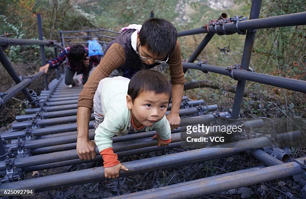Teacher helps his 3-year-old boy climb the steel ladder on the cliff on November 19, 2016 in Liangshan Yi Autonomous Prefecture, Sichuan Province of...