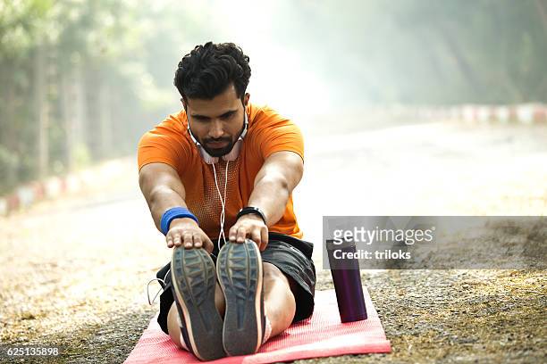man stretching on yoga mat at park - touching toes stock pictures, royalty-free photos & images