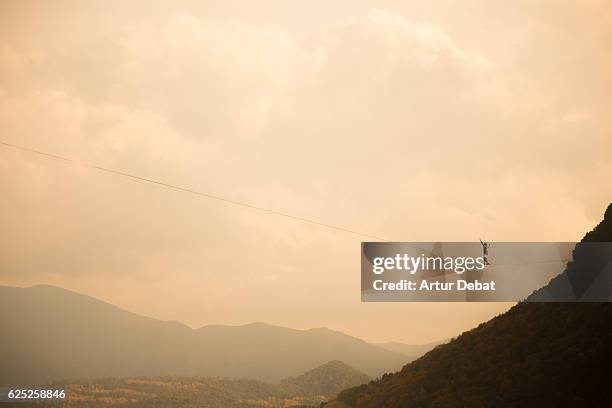 Tightrope walker in a stunning outdoor nature walking between two cliffs over the nature with nice sky.