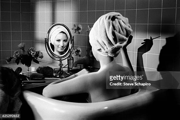 Portrait of actress & musician Barbra Streisand as she sits, her back to the camera, in a bathtub and smiles into a small mirror, Beverly Hills,...