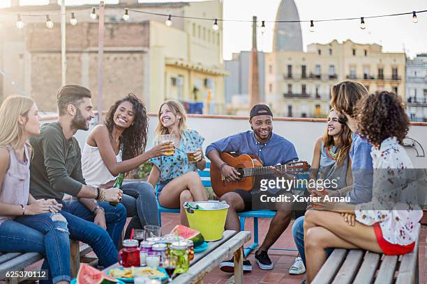 cheerful man playing guitar for friends on terrace - balcony party stock pictures, royalty-free photos & images