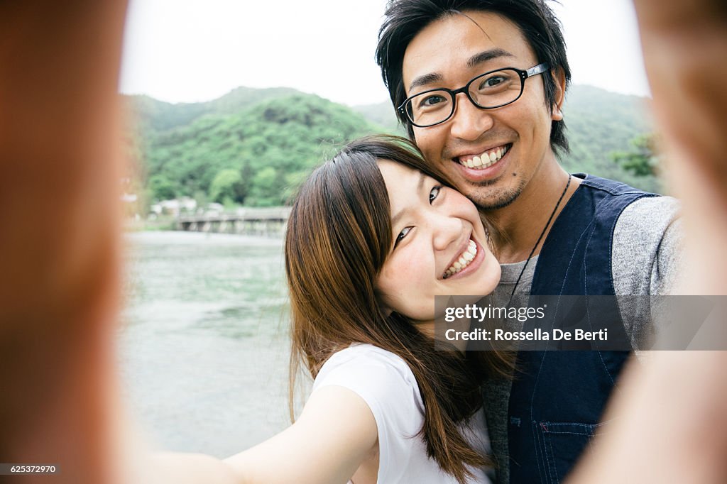 Cheerful Japanese couple taking selfie outdoors in a park