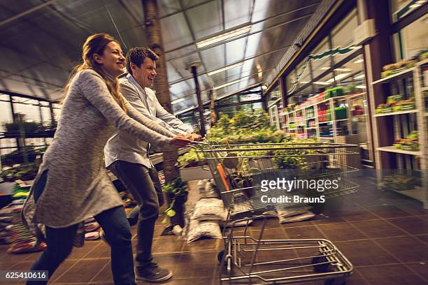 happy couple having fun with shopping cart in garden house. - man pushing cart fun play stock pictures, royalty-free photos & images