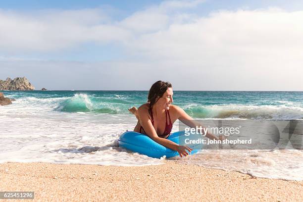 young woman in a blue rubber ring enjoying the beach - lands end cornwall stock pictures, royalty-free photos & images