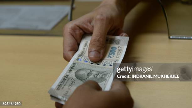 Bank staff member hands Indian 500 rupee notes to a customer on November 24 in the wake of the demonetisation of old 500 and 1000 rupee notes in...