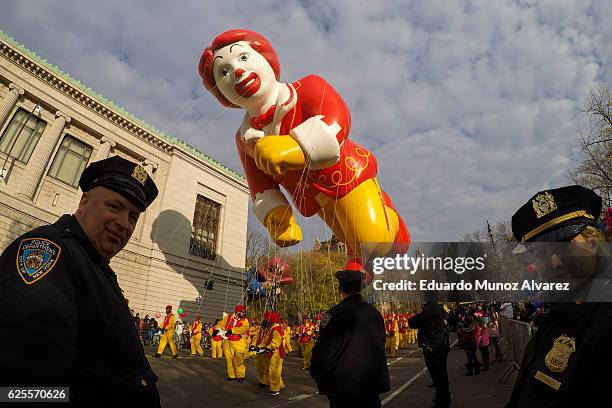 Officers stand guard as revellers holding a Ronald MacDonald balloom walk down Central Park West during the 90th Macy's Annual Thanksgiving Day...