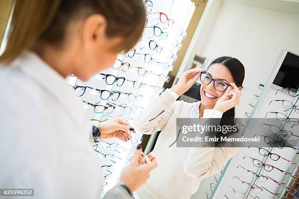 woman trying on eyeglasses in optical shop - bril brillen en lenzen stockfoto's en -beelden