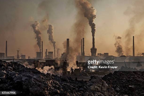 Smoke billows from a large steel plant as a Chinese labourer works at an unauthorized steel factory, foreground, on November 4, 2016 in Inner...