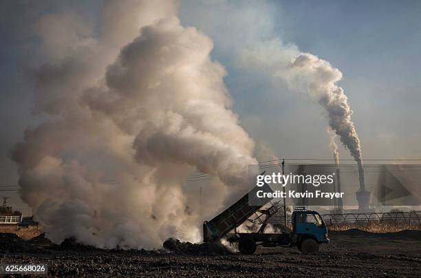 Chinese labourer unloads waste coal and stone as smoke and steam rises next to an unauthorized steel factory on November 3, 2016 in Inner Mongolia,...