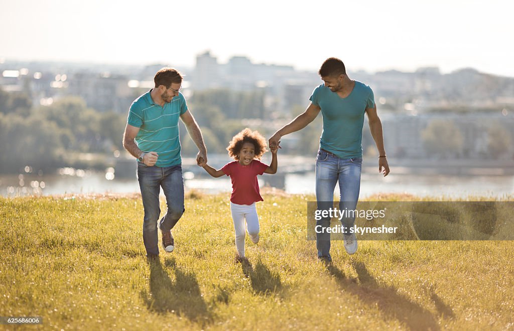 Gay parents running in the park with their adopted daughter.