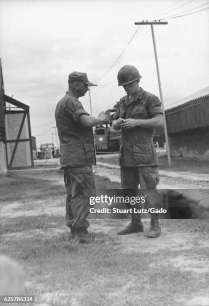 Photograph of two United States army servicemen in combat uniforms speaking to each other on their base, Vietnam, 1967. .