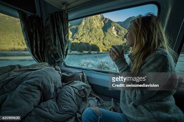 young woman in camper looks through window, new zealand - motor home winter stock pictures, royalty-free photos & images
