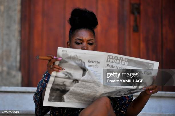 Woman smokes a cigar as she reads the newspaper in a street of Havana, on November 26 the day after Cuban revolutionary leader Fidel Castro died aged...