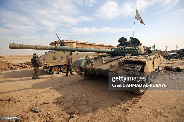 Shiite fighters from the Hashed al-Shaabi walk next to an Iraqi T-72 tank in the village of Baylunah, southwest of Mosul, on November 27 during an...