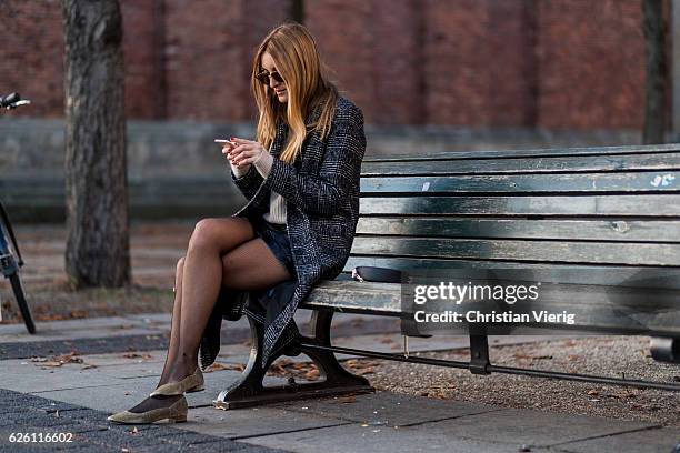 Sofia Grau sitting on a bench writting a text message wearing a black plaid checked Urban Outfitters wool coat, a white creme &other stories jumper,...