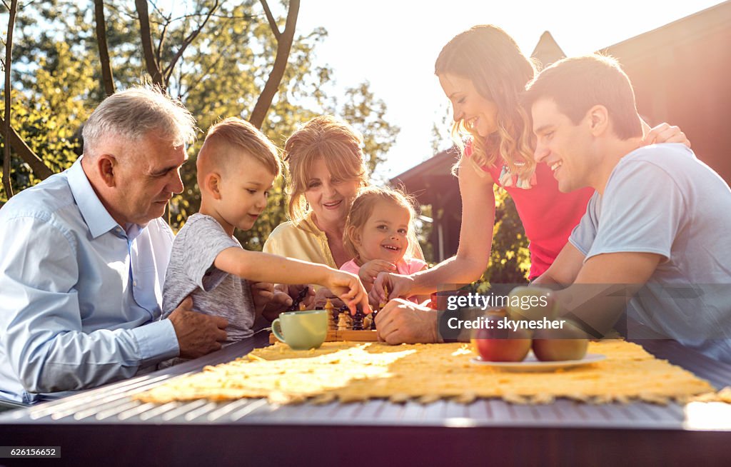 Happy multi-generation family playing chess in the garden.