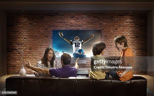 family with children watching american football game on tv - tv family stockfoto's en -beelden