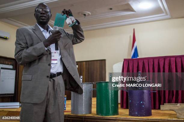 An IEC official shows an electoral document of incumbent president Yahya Jammeh next to the ballot boxes with the colours of the three parties...