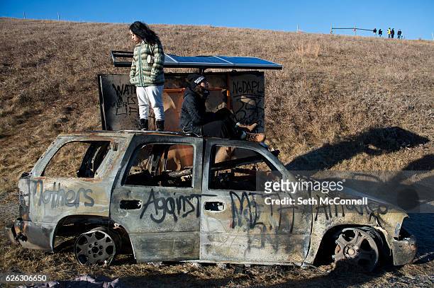 Florcy Romero, left, and Ewok Gia stand and sit on the top of a burned out car along Highway 1806 near the Oceti Sakowin Camp on the Standing Rock...