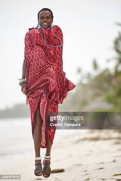 eleganter maasai-mann springt am strand von sansibar. - folkloric stock-fotos und bilder