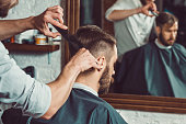 The hands of young barber making haircut to attractive man