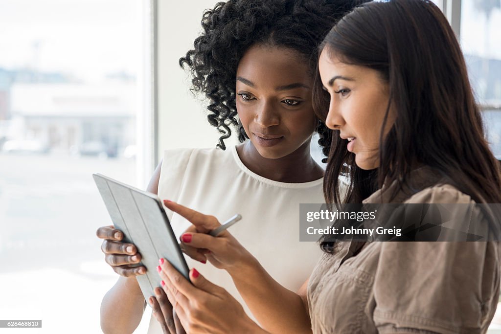 Deux femmes d’affaires tenant une tablette numérique, femme hispanique pointant du verso