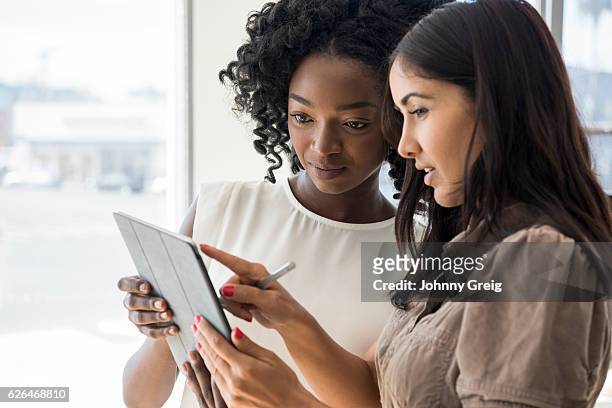 two businesswomen holding digital tablet, hispanic woman pointing - explaining stock pictures, royalty-free photos & images