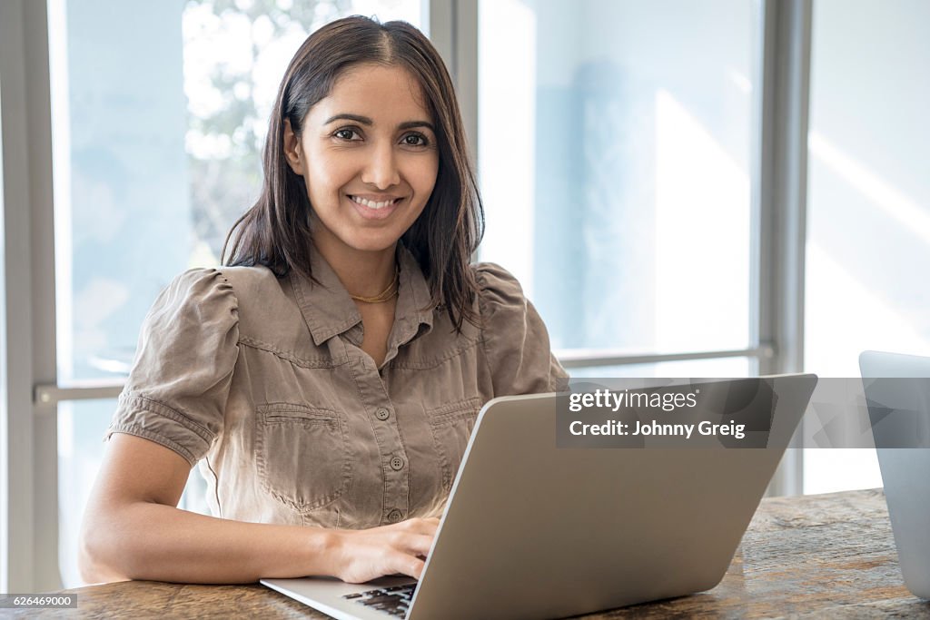 Portrait of Hispanic businesswoman using laptop and smiling