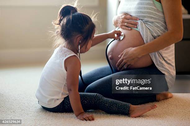 young ethnic daughter holding stethescope up to moms pregnant belly - stomach child stock pictures, royalty-free photos & images