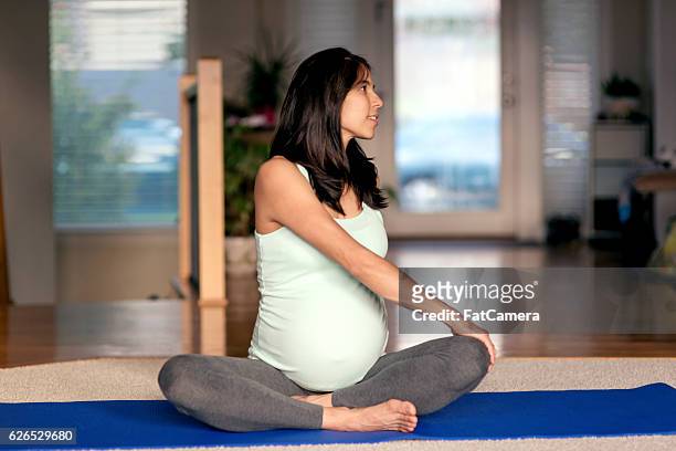 ethnic mother stretching while sitting on yoga mat at home - prenatal yoga stock pictures, royalty-free photos & images