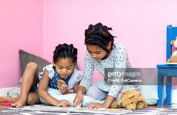 zwei junge afroamerikanische schwestern lesen gemeinsam ein buch - fat twins stock-fotos und bilder