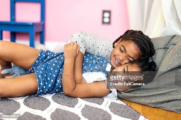 jolie fille afro-américaine chatouillant sœur cadette sur le sol - fat twins photos et images de collection