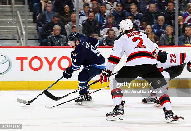 Andrew Copp of the Winnipeg Jets plays the puck down the ice as Kyle Quincey and John Moore of the New Jersey Devils defend during second period...