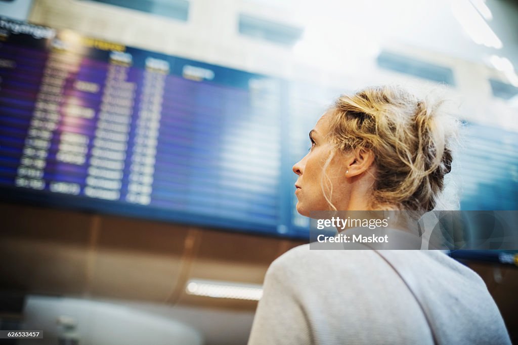 Rear view of businesswoman looking at arrival departure board in airport