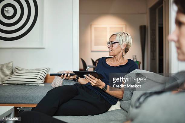 industrial designer using remote control while sitting with colleague on sofa at home - 2015 45 50 stock pictures, royalty-free photos & images