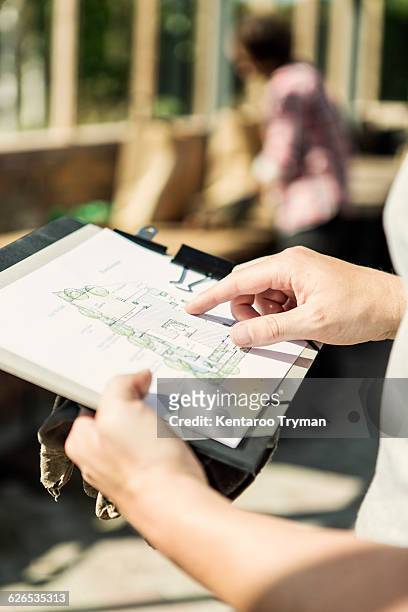 cropped image of man analyzing plan while woman working in background at greenhouse - garden drawing stockfoto's en -beelden