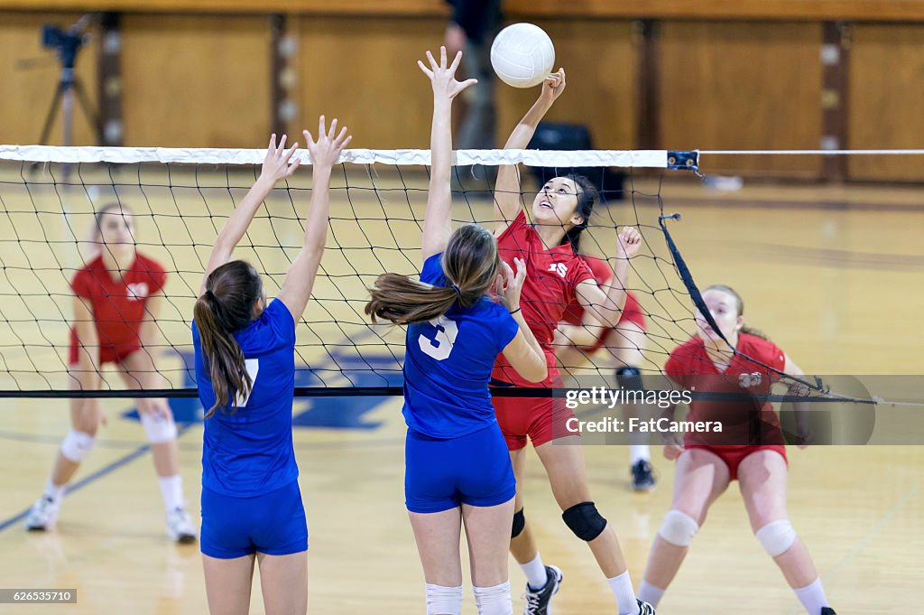 Asian high school volleyball player spikes volleyball against female opponents