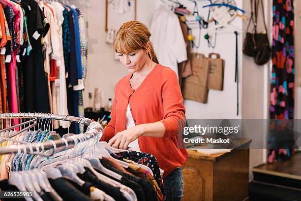 owner arranging clothes on rack while standing at thrift store - fashion store staff stock pictures, royalty-free photos & images