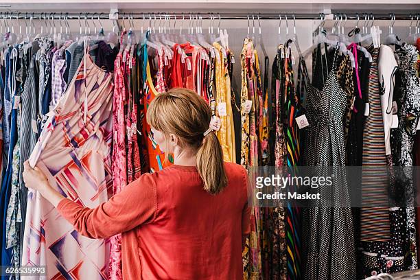 woman looking at dress hanging on rack while standing at store - barra para colgar la ropa fotografías e imágenes de stock