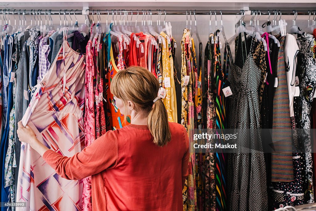 Woman looking at dress hanging on rack while standing at store