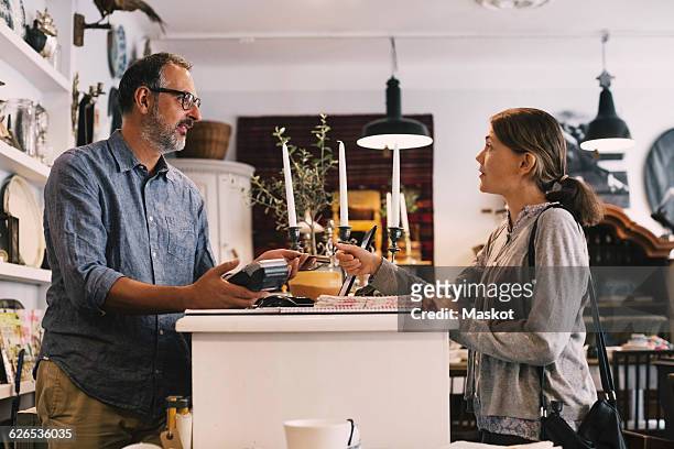 owner giving credit card to female customer while standing at shop counter - man in antique shop stock pictures, royalty-free photos & images
